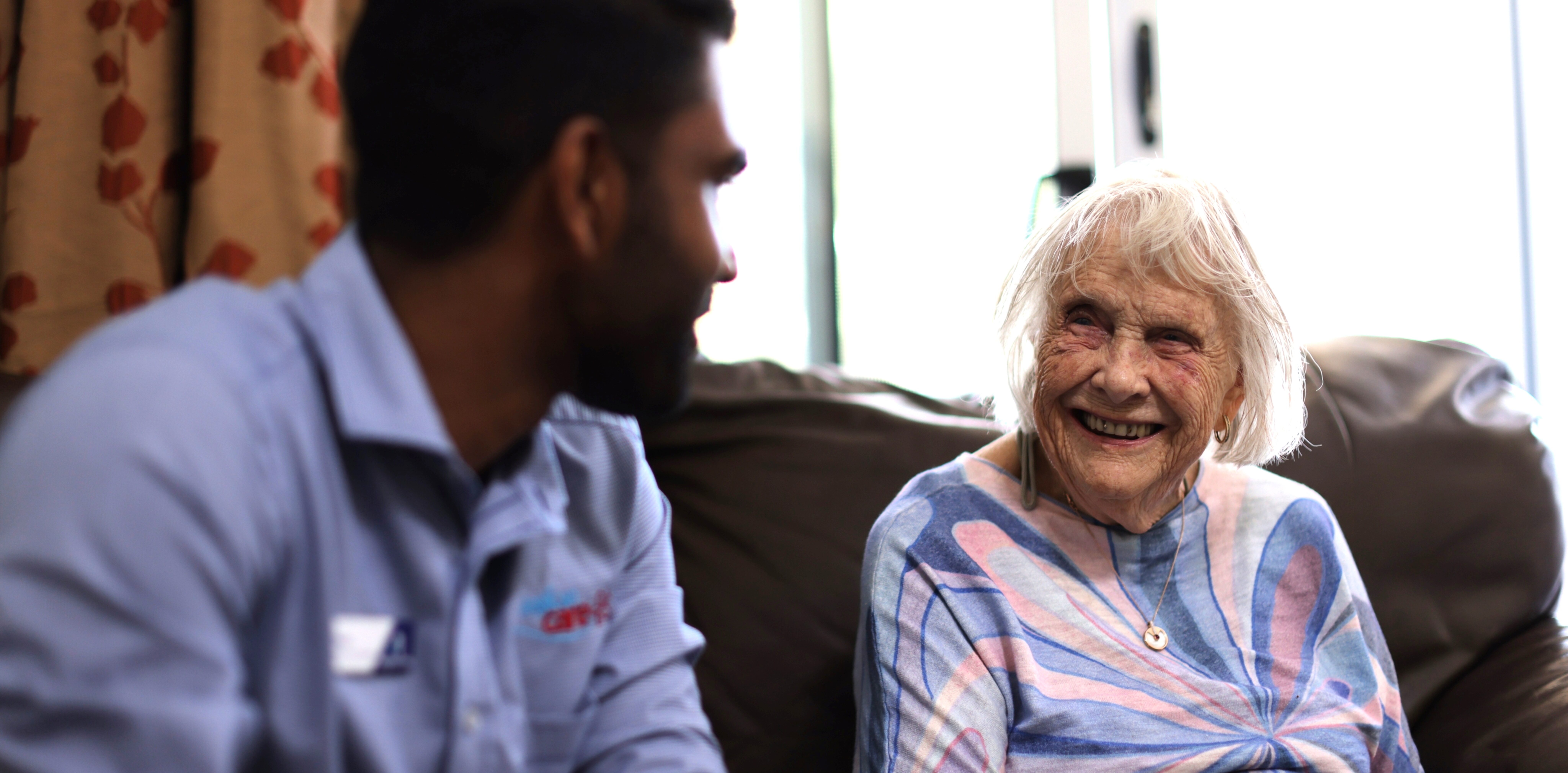 A care worker having a friendly conversation with an older woman seated on a couch.